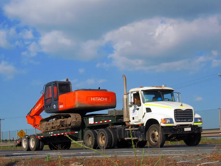 Camión Mack transportando una excavadora sobre cama baja.
