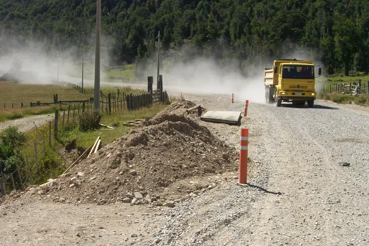 Camión tolva en un camino de ripio junto a una obra vial.
